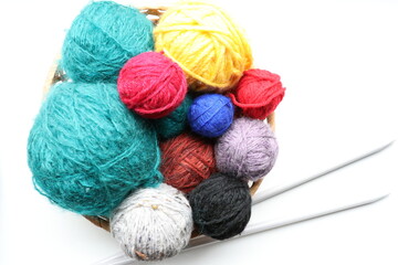 Top view of multicolored yarn in basket and knitting needles on white background 