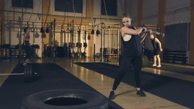 Fitness woman hitting tire with sledgehammer. Slow motion