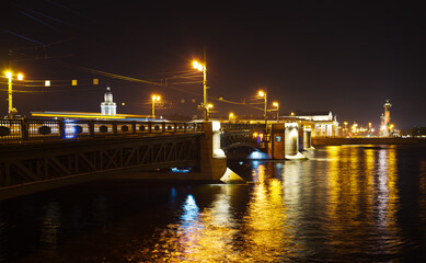 Fototapeta na wymiar St. Petersburg at night. View of the Palace Bridge, the Neva River with color reflection and the embankment of Vasilievsky Island with Rastral Columns. Beautiful evening cityscape