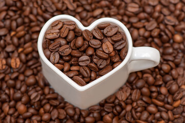 Coffee beans. White mug heart filled with coffee beans on coffee beans background. Close up