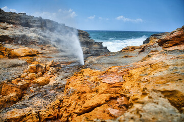 A small geyser on the very edge of a rocky coast by the sea.