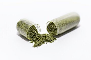 Close-up one opened soft capsule pill with green herbal powder on white background. medicine supplement vitamin