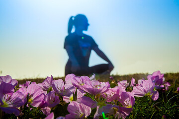 Fototapeta na wymiar Spring flowers Pink Evening Primrose (Oenothera speciosa) and the silhouette of a woman sitting in a lotus position, selective focus