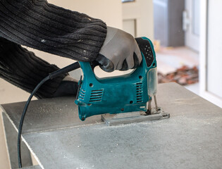 male hands of construction worker sawing and cutting parts with an electric hand jigsaw from  panel. the process of cutting building board for interior decoration with an electric jigsaw