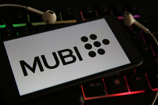 Viersen, Germany - March 1. 2021: Closeup of mobile phone screen with logo lettering of streaming service mubi on laptop keyboard