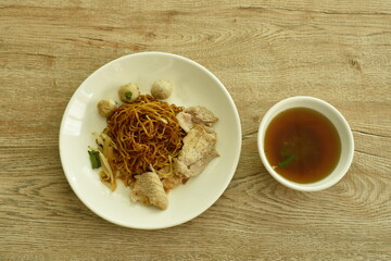 dried Chinese yellow egg noodles topping slice boiled  pork and meatball dressing black sweet soybean sauce on white dish with soup