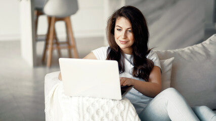 Makes online purchases on the computer. The housewife is sitting at home. Young woman online training on a laptop.
