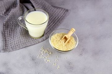 Rice milk in a glass mug and a rice grains in a bowl on a grey background. Vegetable milk. Vegan...