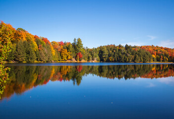 Fall colours and a clear blue sky reflecting off of a calm blue lake - Gatineau Park, Quebec, Canada