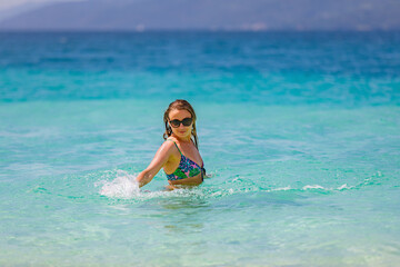 Young beautiful girl splashes in the blue water of the ocean.