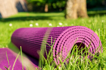 Rolled Yoga mat on green grass with sunlight in summer, close up. Outdoor sport concept