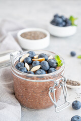 Chocolate chia pudding with blueberry, almonds and mint on top in a glass jar on a gray concrete background. Healthy food. Copy space.