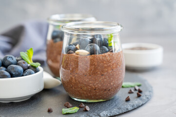 Chocolate chia pudding with blueberry, almonds and mint on top in a glass jar on a gray concrete background. Healthy food. Copy space.