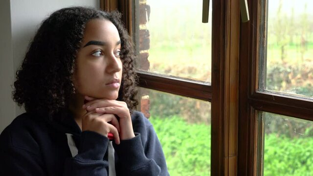 Beautiful mixed race biracial African American girl teenager young woman using her cell phone looking out of a window looking sad then happy