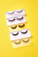 Different false eyelashes on a trendy bright yellow background. Beauty pop art, Makeup accessories. Cosmetics products for women, lashmaker concept. Bright colorful backdrop