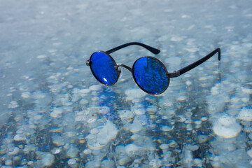 blue sunglasses lie on transparent ice
