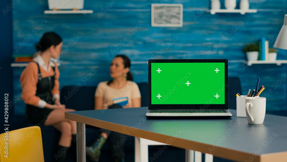Poster laptop computer with mock up green screen chroma key standing on desk while in background two women 