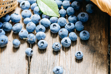 Freshly picked blueberries scattered on a rustic wooden table. Juicy and fresh blueberries with green leaves. Concept for healthy eating and nutrition.