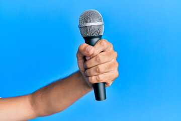 Hand of hispanic man holding microphone over isolated blue background.