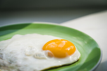 A freshly cooked hot fried egg sits on a green plate. Healthy breakfast. Close-up.