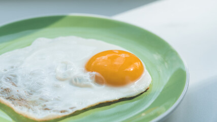 A freshly cooked hot fried egg sits on a green plate. Healthy breakfast. Close-up.