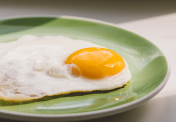 A freshly cooked hot fried egg sits on a green plate. Healthy breakfast. Close-up.
