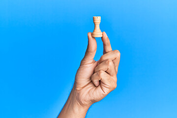 Hand of hispanic man holding tower chess piece over isolated blue background.