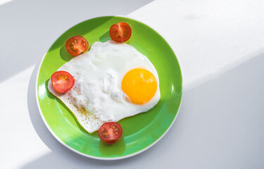 A freshly cooked hot fried egg and cherry tomatoes cut in half lie on a green plate. Healthy breakfast. Close-up. View from above.