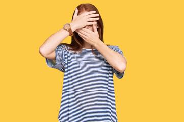 Young read head woman wearing casual clothes and glasses covering eyes and mouth with hands,...