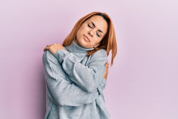Hispanic young woman wearing casual turtleneck sweater hugging oneself happy and positive, smiling confident. self love and self care