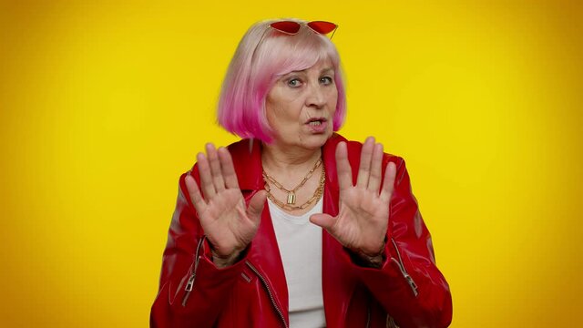 I am not guilty. Confused senior old granny woman with pink hair pointing fingers himself ask say who me no thanks i do not need it isolated on yellow studio background. Elderly grandmother pensioner