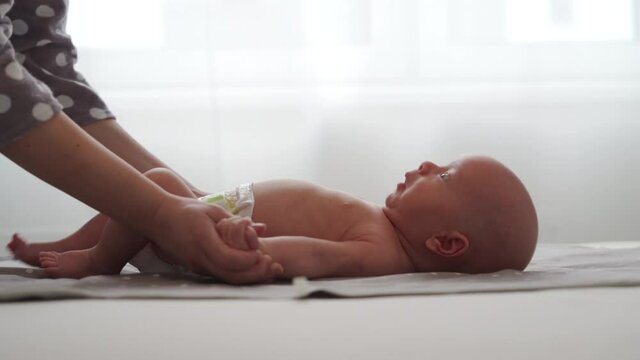 Mother with baby boy doing exercise simple exercises to make baby bones and muscles stronger, newborn infant lying on bed against the window. High quality 4k footage