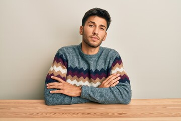 Young handsome man wearing casual sweater sitting on the table relaxed with serious expression on...