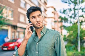 Young latin man with serious expression talking on the smartphone walking at the city.