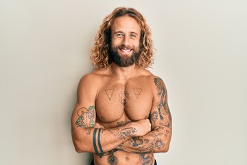 Handsome man with beard and long hair standing shirtless showing tattoos happy face smiling with...