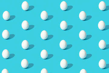 Pattern made of white eggs with hard light on blue background. Minimal Easter holiday concept.