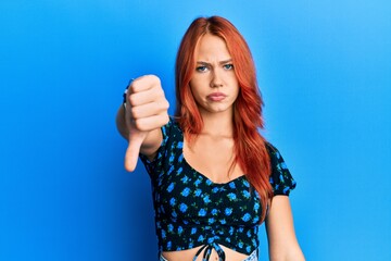 Young beautiful redhead woman wearing casual clothes over blue background looking unhappy and angry...