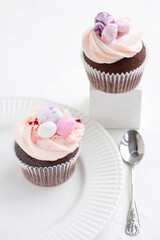 Two Easter chocolate cupcakes with caramel filling and decoration of small Easter eggs from marzipan on a white porcelain plate. Selective focus