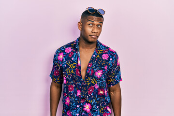 Young black man wearing hawaiian shirt and sunglasses smiling looking to the side and staring away thinking.