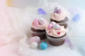 Three Easter chocolate cupcakes with caramel filling and decoration of small Easter eggs from marzipan on the white background. Selective focus