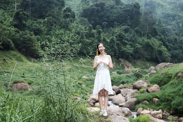 Naklejka na ściany i meble Beautiful asian female in white dress is standing on the rock and stream in the tropical forest