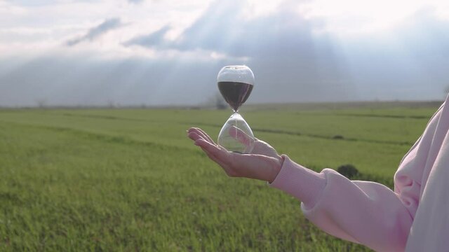 Outdoors holding a glass hourglass in a female hand. Time is a fleeting concept.