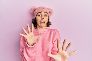 Young brunette woman wearing cute wool cap afraid and terrified with fear expression stop gesture with hands, shouting in shock. panic concept.
