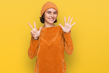 Young hispanic woman wearing casual clothes and wool cap showing and pointing up with fingers number eight while smiling confident and happy.