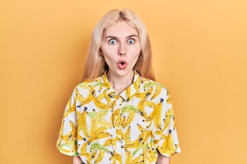 Beautiful caucasian woman with blond hair wearing colorful shirt scared and amazed with open mouth...