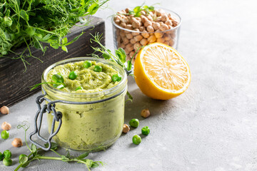 Obraz na płótnie Canvas Avocado hummus in a glass jar with chickpeas, green peas, spices on gray background. Healthy vegan dip. copy space.