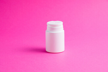 White jar of pills or vitamins on a pink paper background. Medicine on background with copy space.