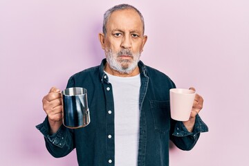 Handsome senior man with beard holding coffee and milk relaxed with serious expression on face....