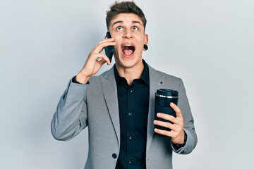 Young caucasian boy with ears dilation using smartphone and drinking a cup of coffee angry and mad screaming frustrated and furious, shouting with anger looking up.