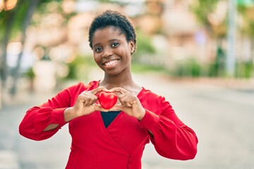 Young african american woman smiling happy holding heart standing at the city.